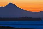 Silhouetted by the setting sun at sunset, Mount Taranaki dominates the region of Taranaki with its 2,518 metre (8,261 feet) height along the West Coast of the North Island of New Zealand.